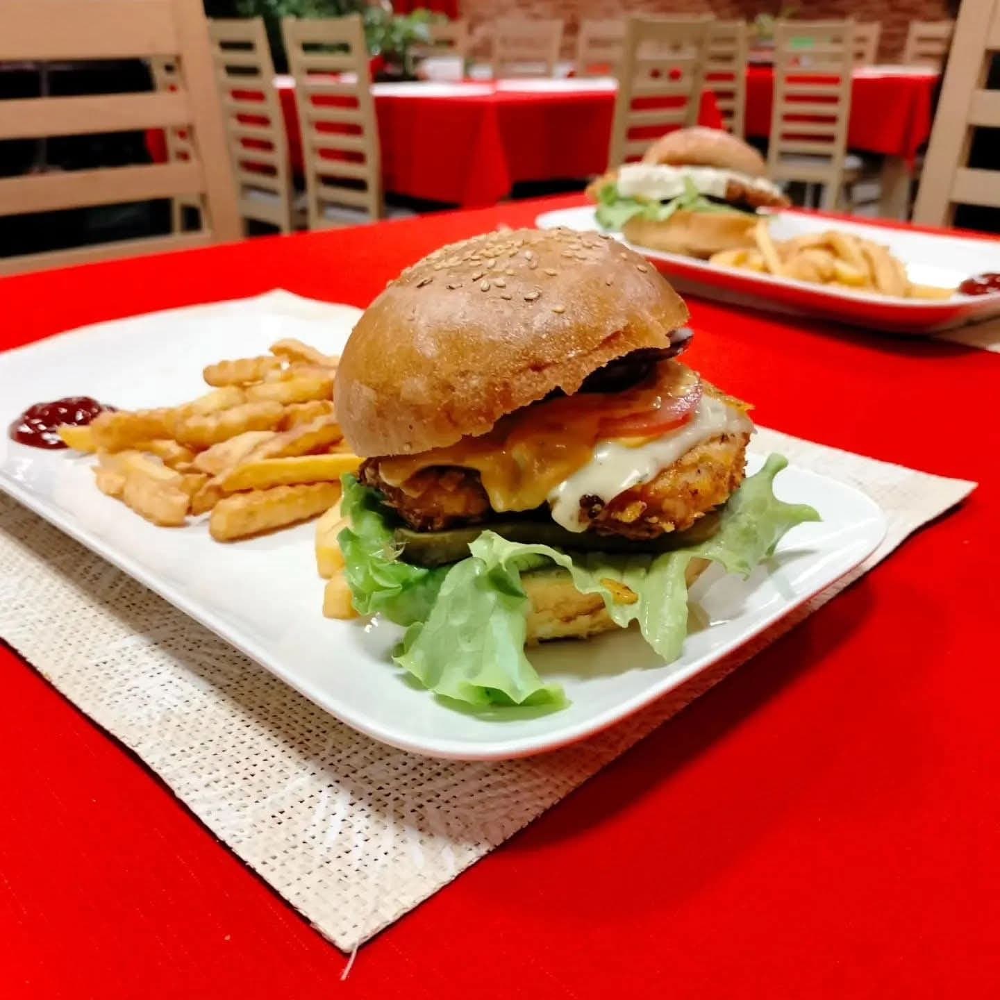 Burger z panierowanym kurczakiem, serem, sałatą i pomidorem, podany z frytkami w sali restauracyjnej